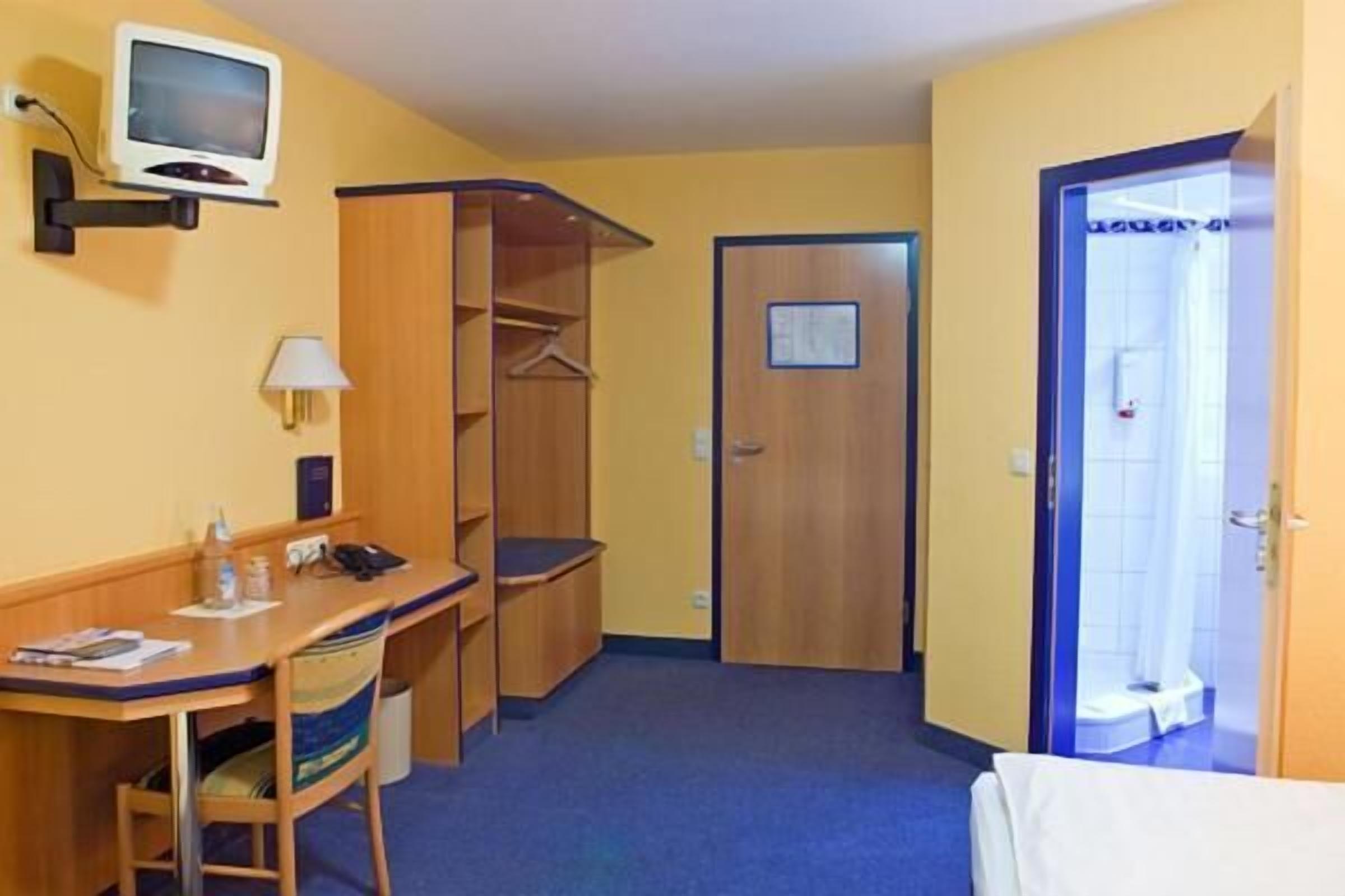 Ein Hotelzimmer mit Schreibtisch, Stuhl, Kleiderschrank und Dusche.
