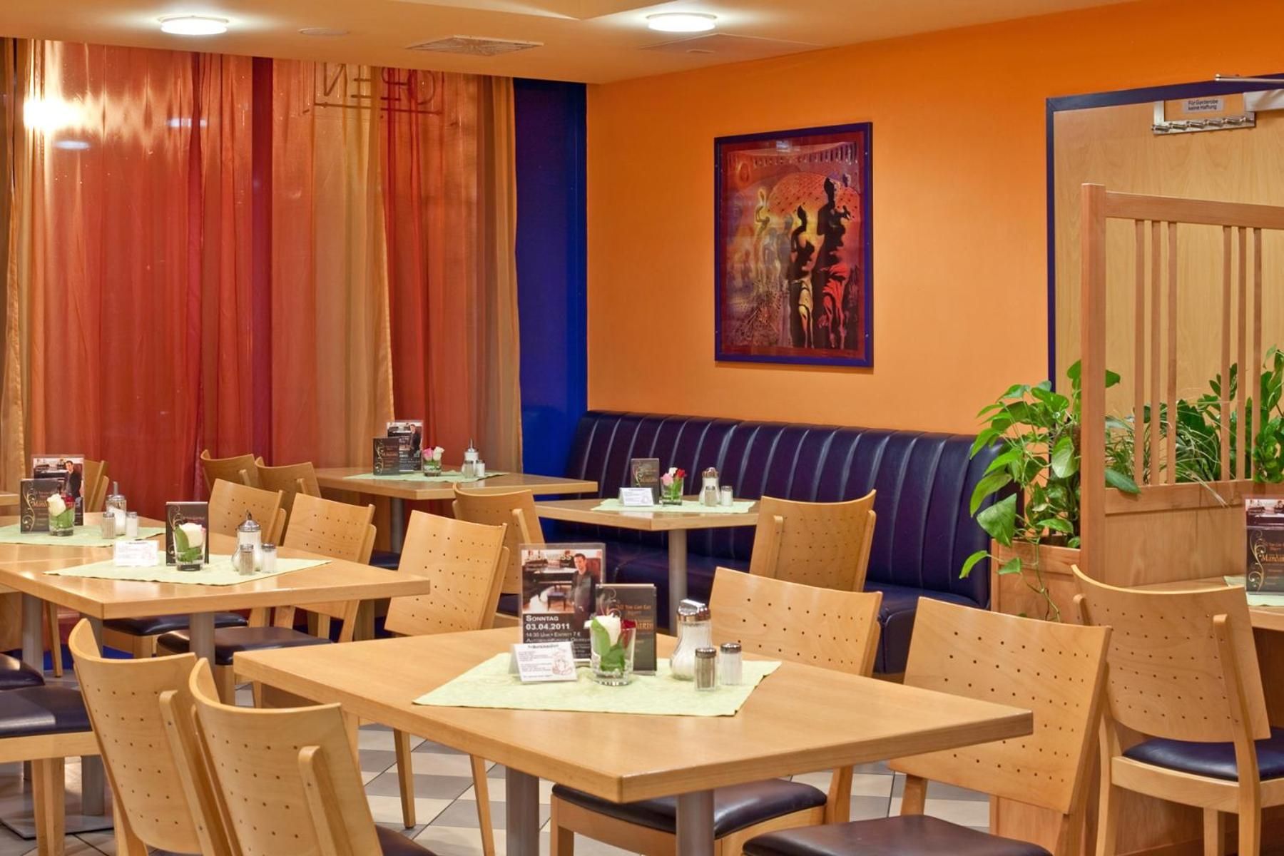A restaurant interior with multiple wooden tables and chairs, a blue cushioned bench, and a framed artwork on the wall.