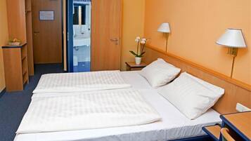Une chambre d’hôtel avec deux lits, un bureau, une chaise, une table de chevet, une lampe et une petite table sur laquelle est posée une plante.