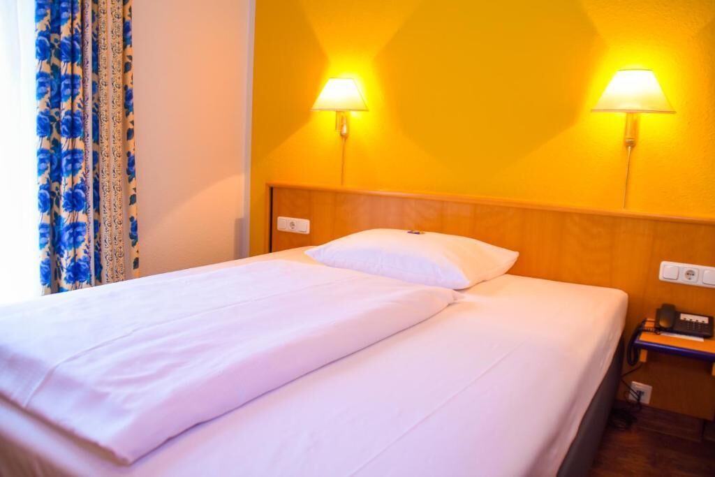 Habitación de hotel con cama, dos lámparas de pared, teléfono e enchufe.