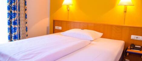 Habitación de hotel con cama, dos lámparas de pared, teléfono e enchufe.