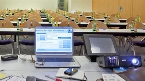 A conference room with tables, chairs, laptops, a projector, and a microphone.