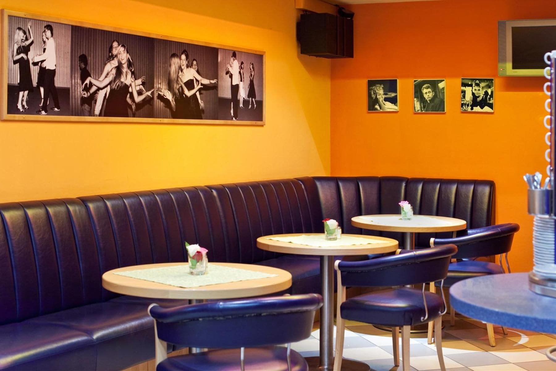 A restaurant with a booth seating area, round tables, and black leather booths.