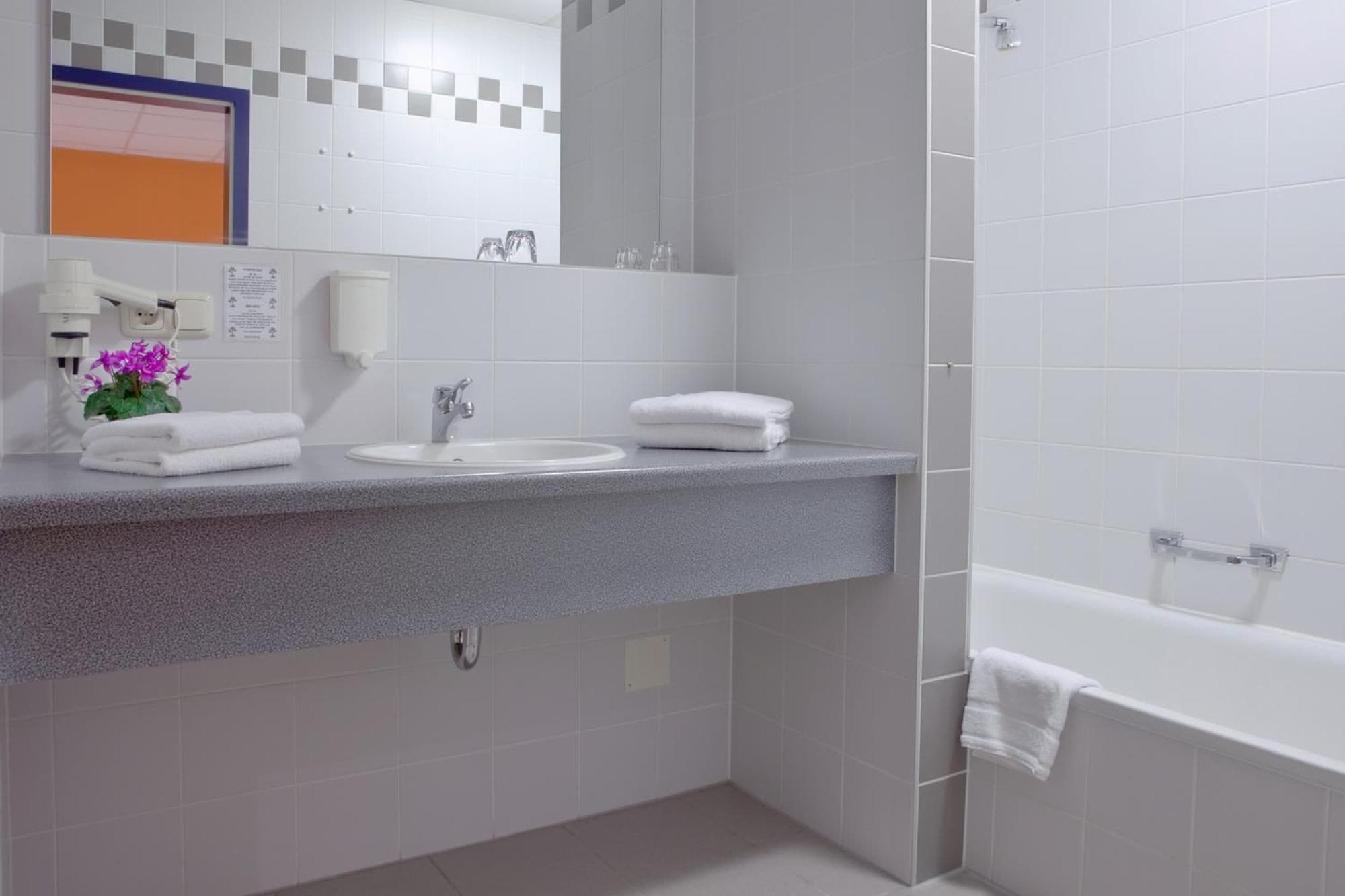 Een moderne badkamer met een grijs aanrecht, een wastafel, een spiegel en een bad.