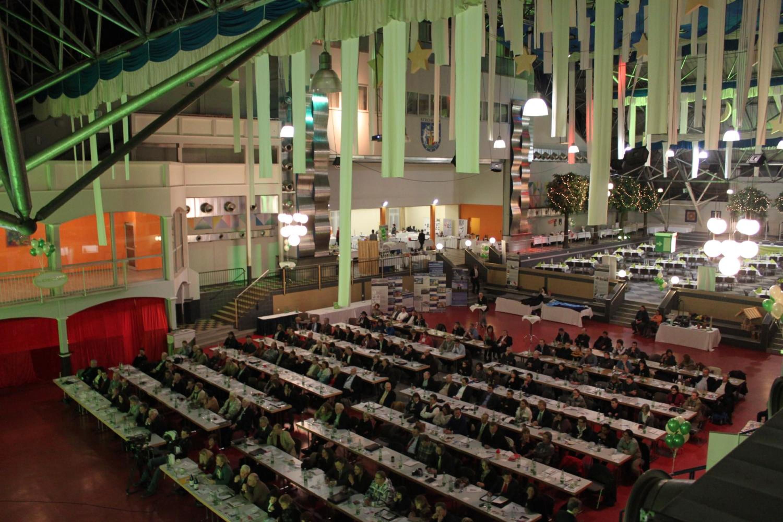 A large indoor venue with multiple rows of tables and chairs, a stage, and a staircase.