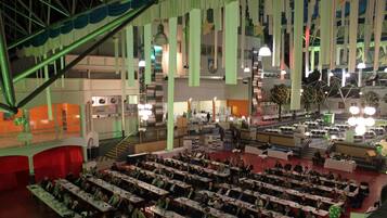 A large indoor venue with multiple rows of tables and chairs, a stage, and a staircase.