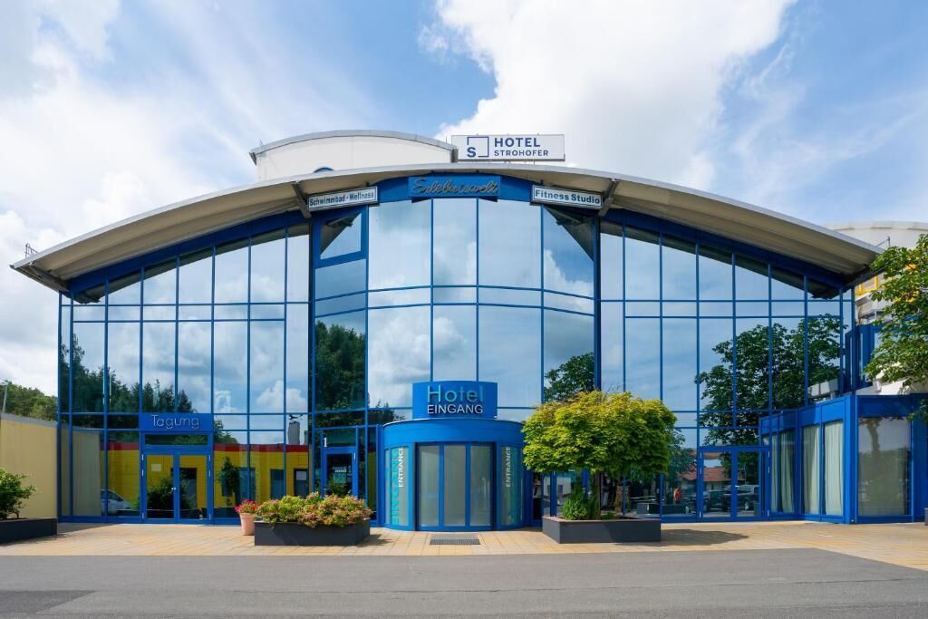 A modern hotel with a curved glass facade, a sign for the hotel, and a fitness studio.