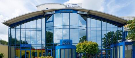 A modern hotel with a curved glass facade, a sign for the hotel, and a fitness studio.