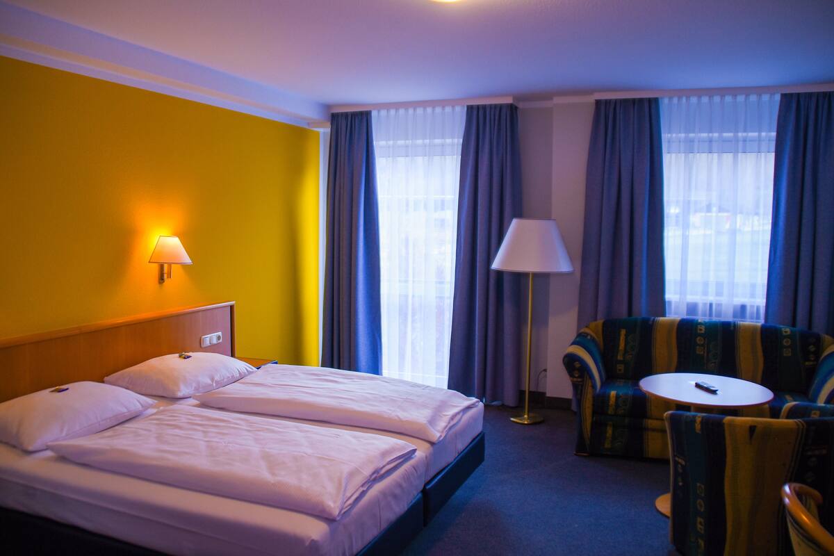 A hotel room with a bed, two bedside tables, a sofa, a chair, and a lamp.
