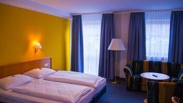 A hotel room with a bed, two bedside tables, a sofa, a chair, and a lamp.
