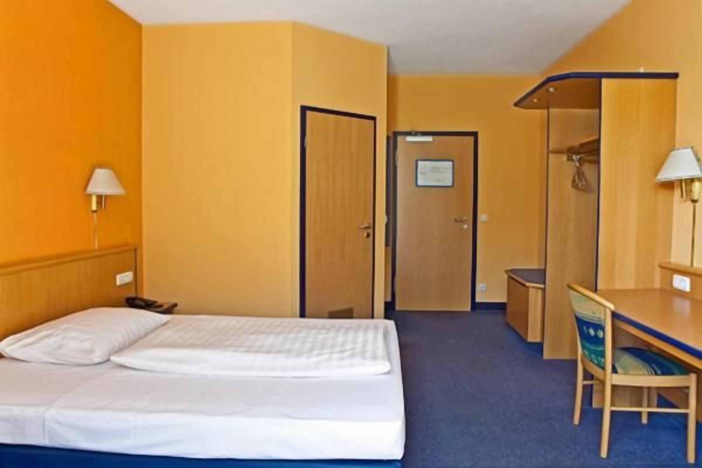 Ein Hotelzimmer mit Bett, Schreibtisch, Stuhl, Lampe und einer Tür.