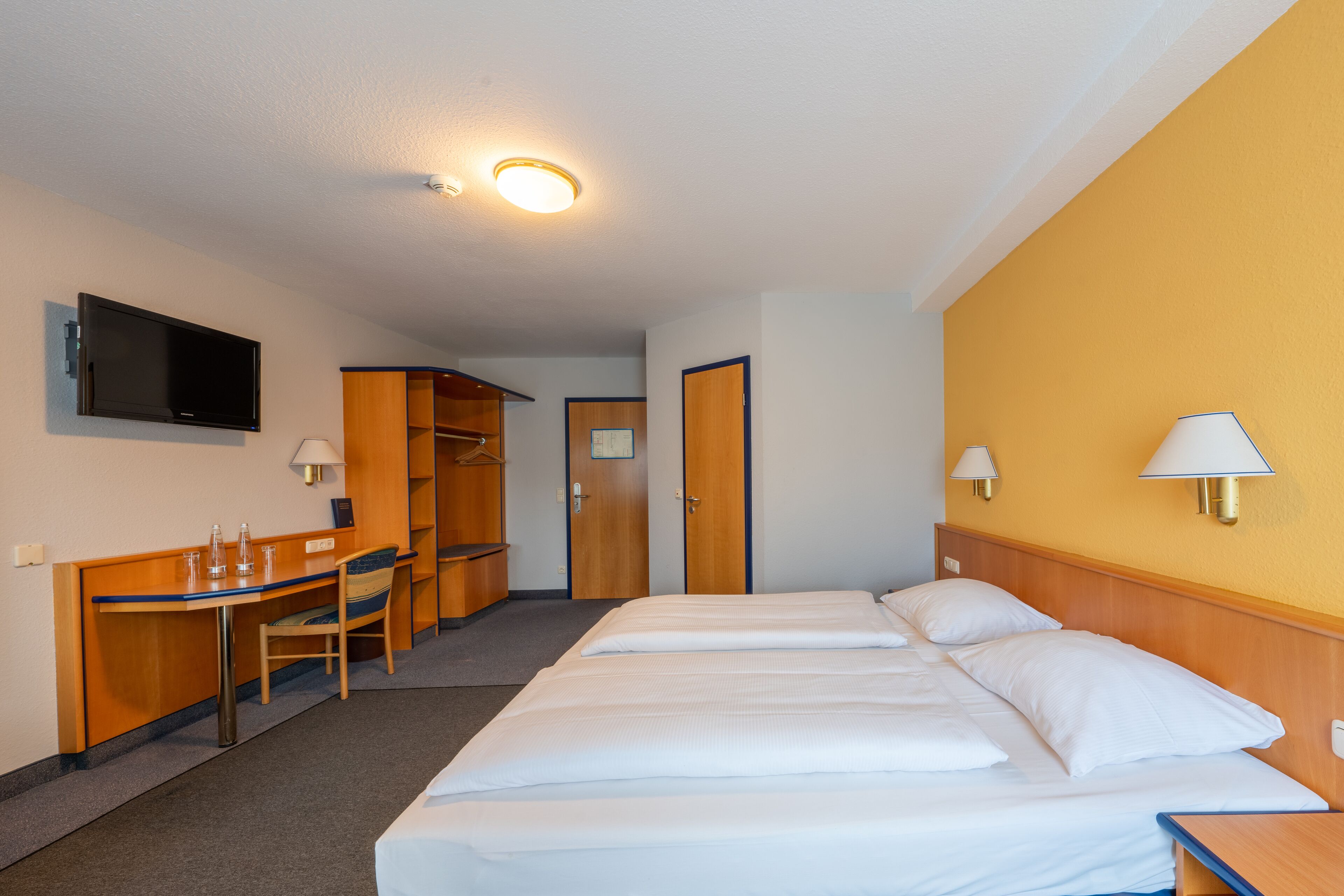 A hotel room with a bed, a desk, a chair, a television, and a wardrobe.