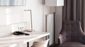 A modern hotel room with a flat-screen TV mounted on the wall, a desk with a lamp, a chair, and a large armchair. - Hotel Rieth (Boeblingen)