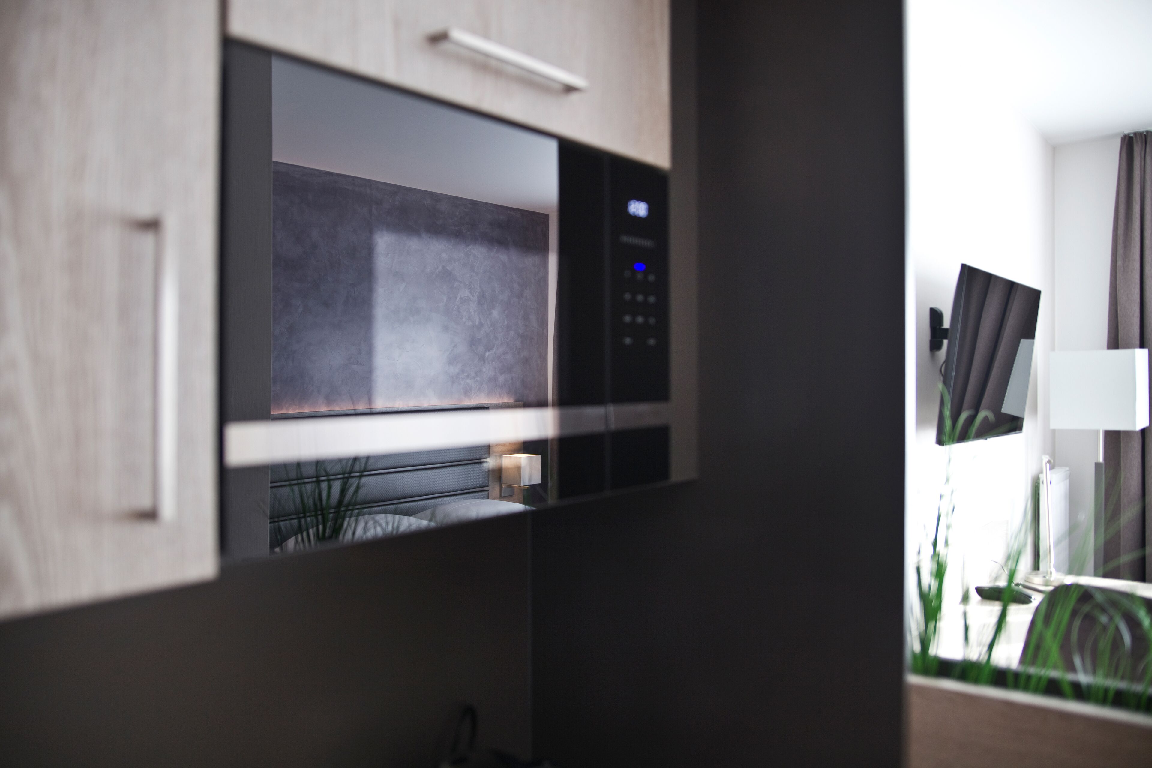 A modern kitchen with a built-in microwave, a wooden cabinet, and a small window.