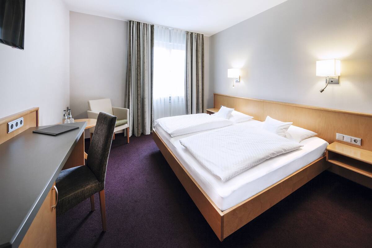 A hotel room with a bed, desk, chair, and a TV mounted on the wall.