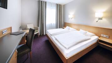 Een hotelkamer met een bed, bureau, stoel en een aan de muur bevestigde televisie.