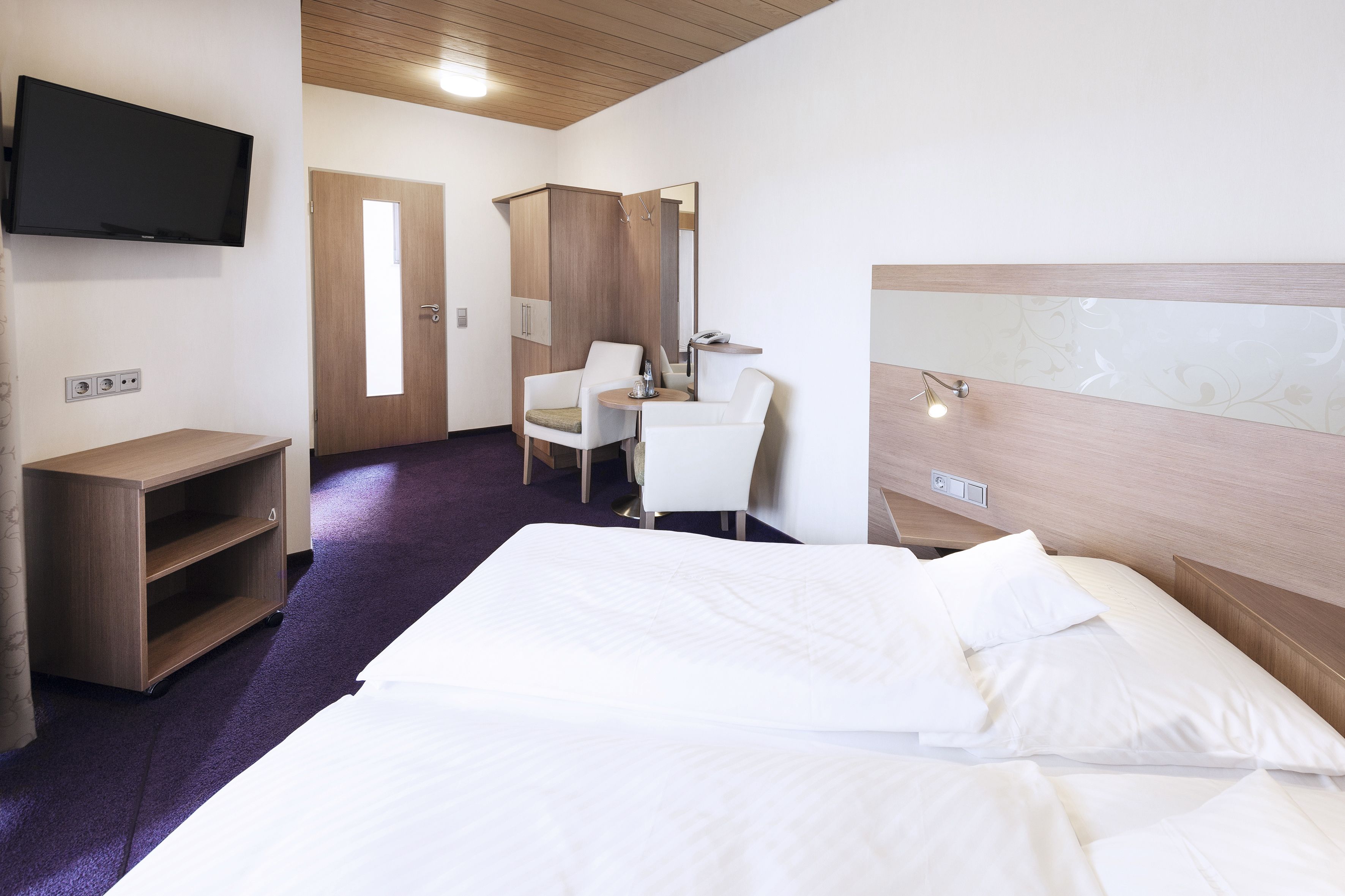A hotel room with a bed, a desk, a chair, a television, and a wardrobe.