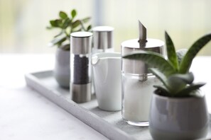 A tray with various containers, including a white pitcher, a jar with a plant, and metallic containers.