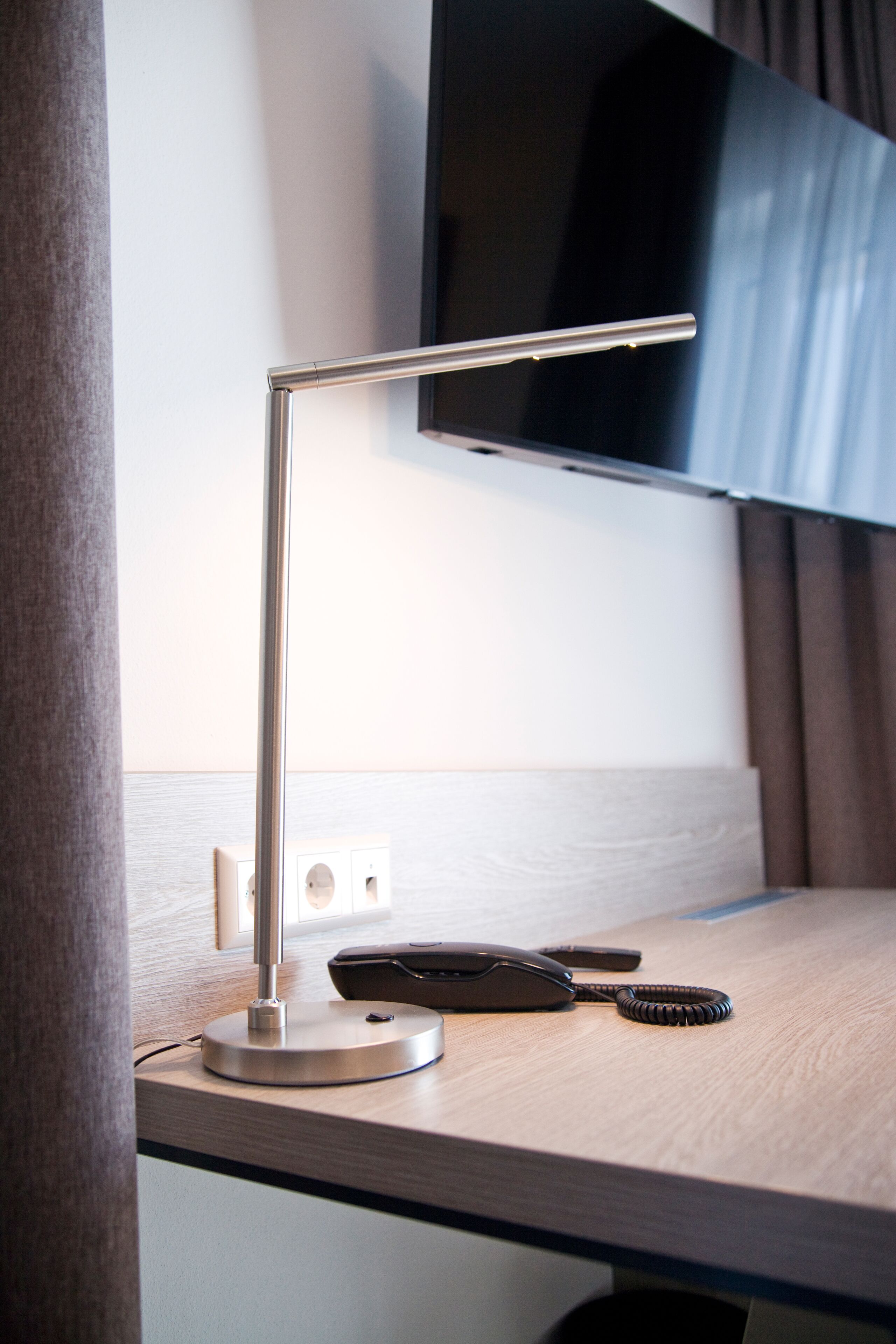 Ein Schreibtisch mit einer modernen Schreibtischlampe, einem Telefon und einem aufgewickelten Kabel.