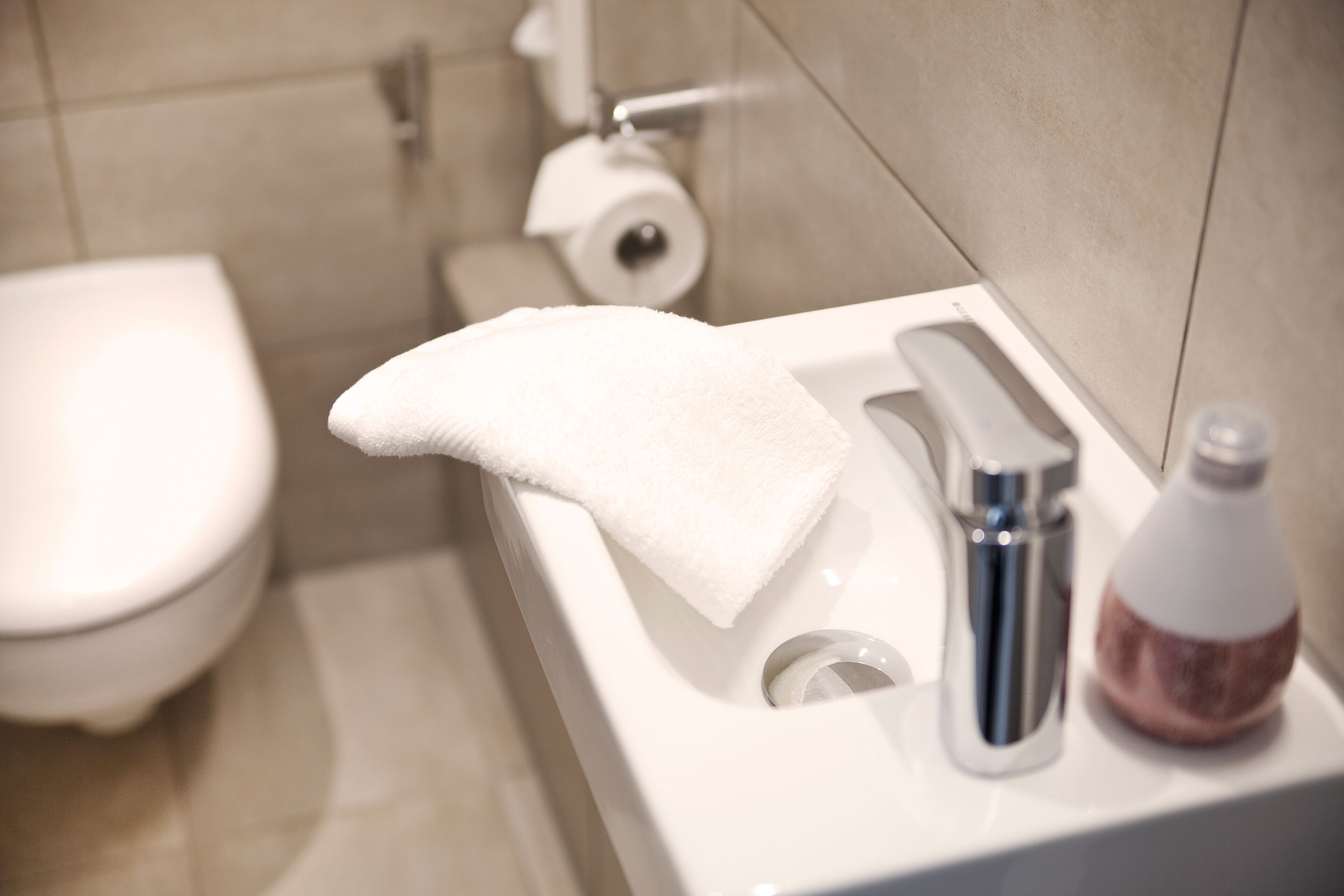 Ein Badezimmer mit einer weißen Toilette, einem Waschbecken mit einem Handtuch und einer Seife.