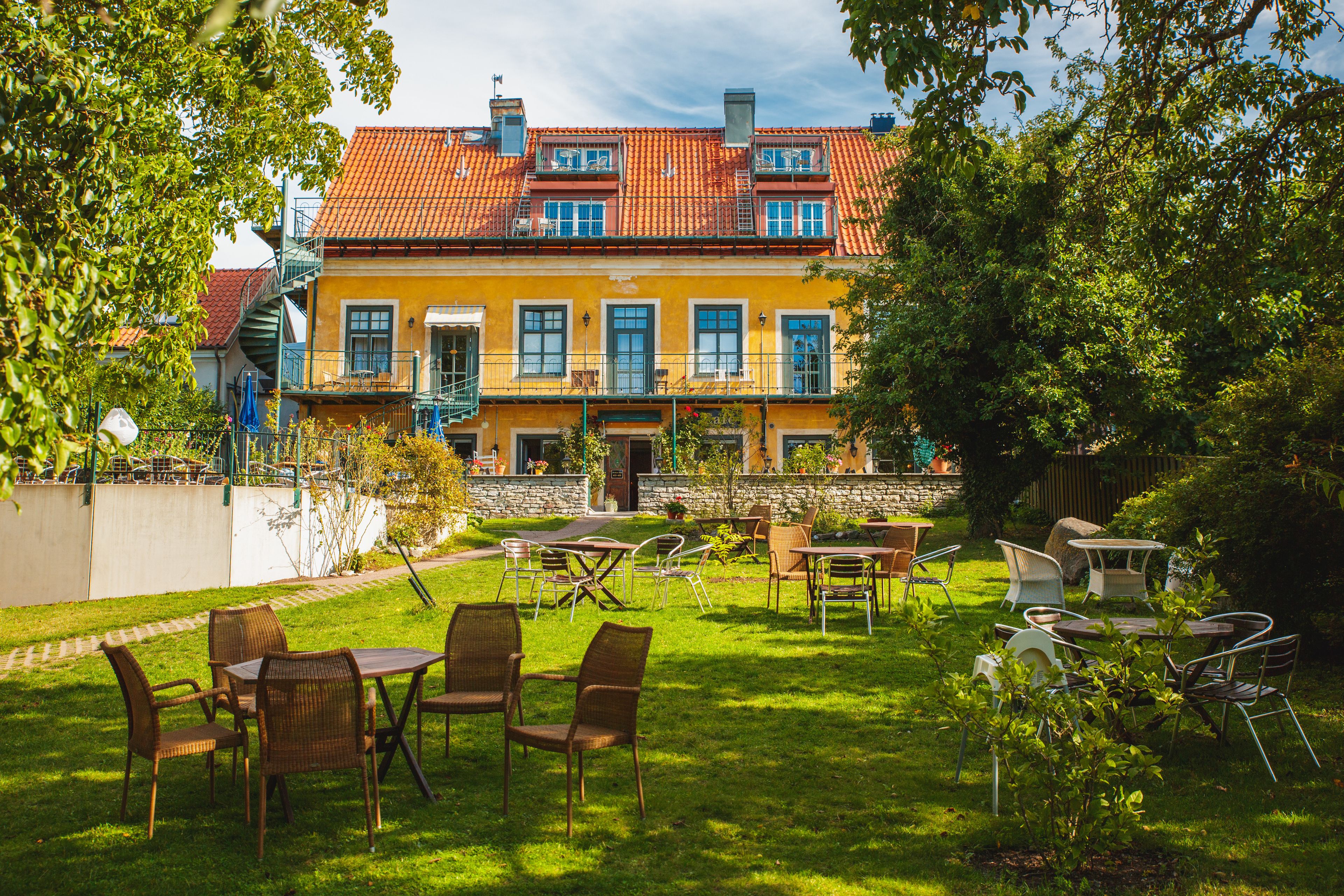 A courtyard with outdoor seating, a yellow building with red tiles, and a stone wall.