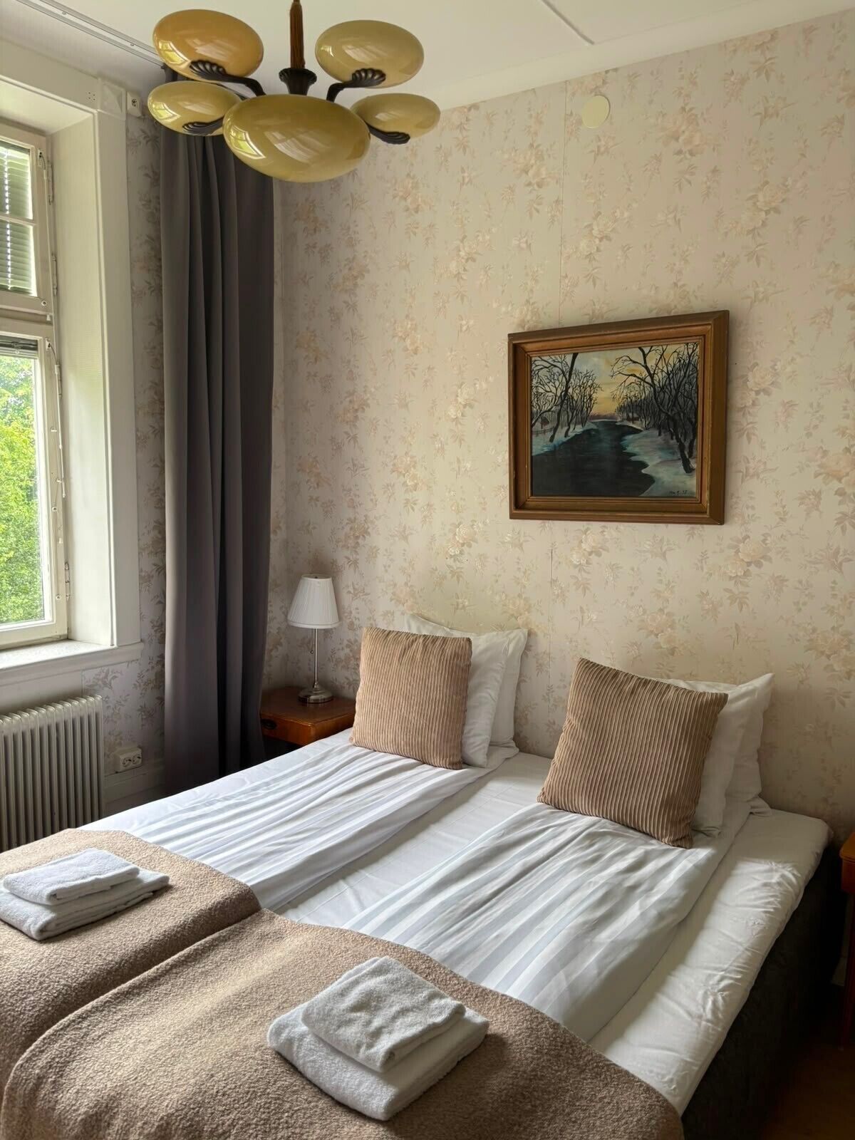 Una habitación de hotel con una cama, un cuadro, una lámpara y una ventana con cortinas.