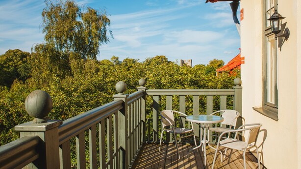 A wooden deck with a railing, a round table, and four chairs. - Hotell Breda Blick (Visby)