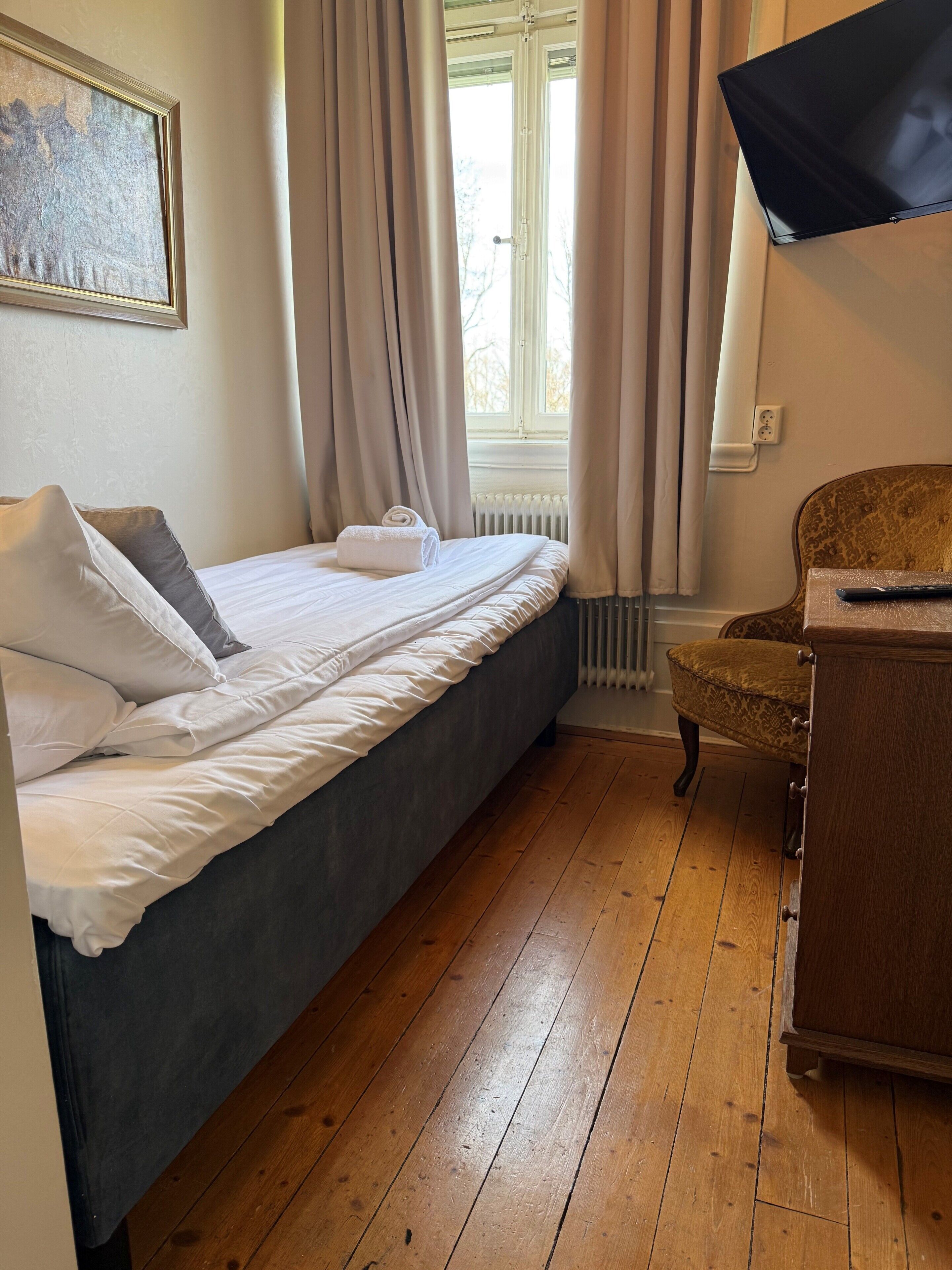 A bedroom with a bed, a chair, a window with curtains, and a radiator.
