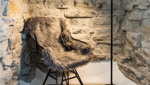A stone-walled room with a fur chair and a floor lamp. - Hotell Breda Blick (Visby)