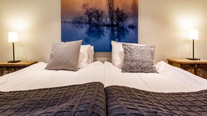 A double bed with patterned pillows, a nightstand with a lamp, and a wall-mounted painting of trees and water. - Hotell Breda Blick (Visby)