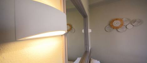 Un baño con espejo, luz empotrada en la pared y un elemento decorativo.