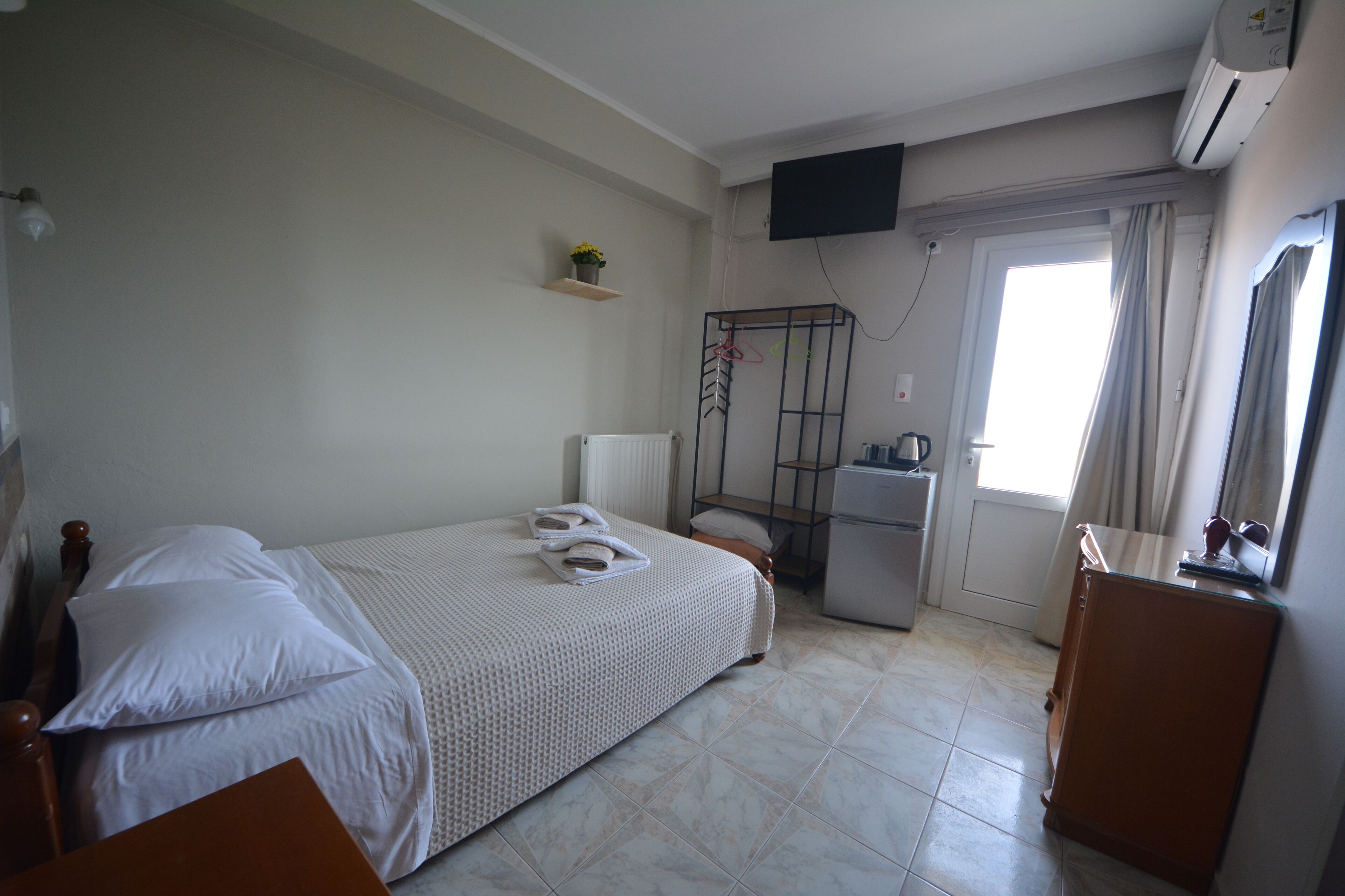 Quarto com cama, uma secretária pequena, radiador, televisão e janela com cortinas.