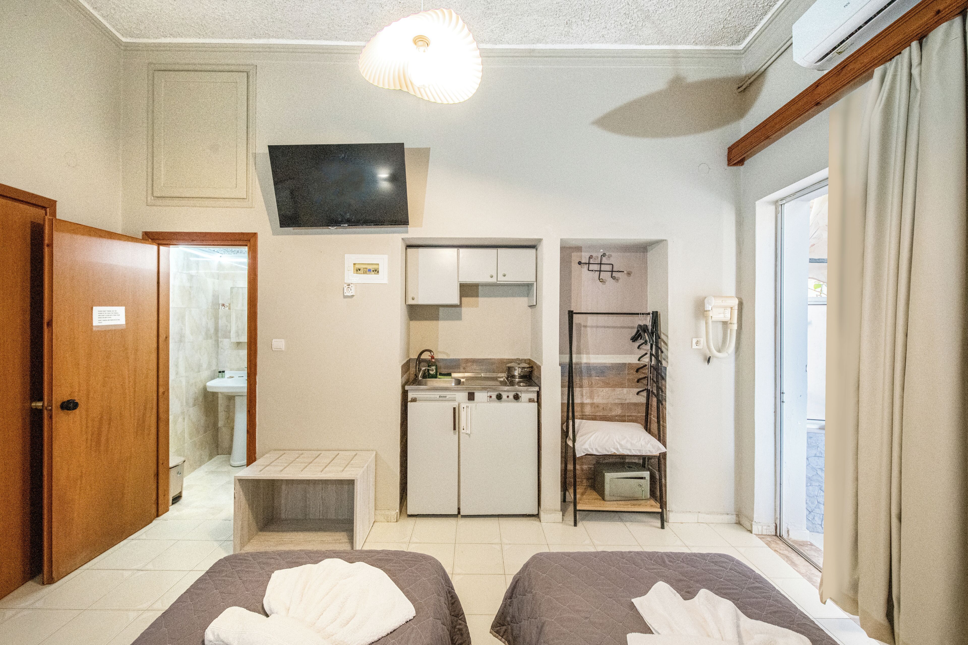 Habitación de hotel con dos camas, televisión, kitchenette y baño.