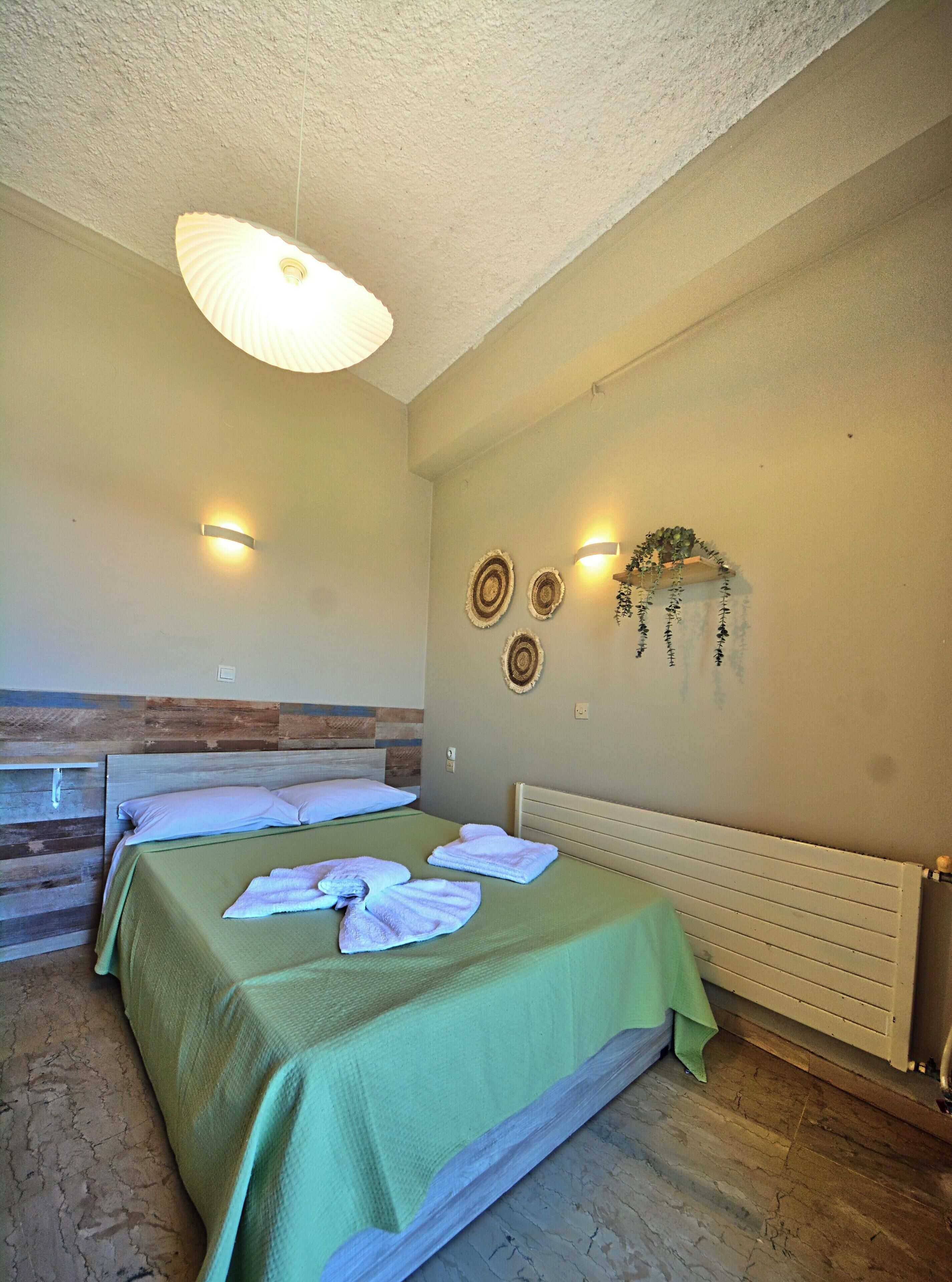 A room with two beds, a ceiling light, wall-mounted sconces, and a decorative wall hanging.