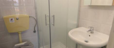 A bathroom with a glass-enclosed shower, a toilet, and a sink.
