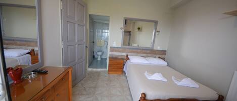 A bedroom with a wooden bed, a dresser, a mirror, and a bathroom visible through an open door.