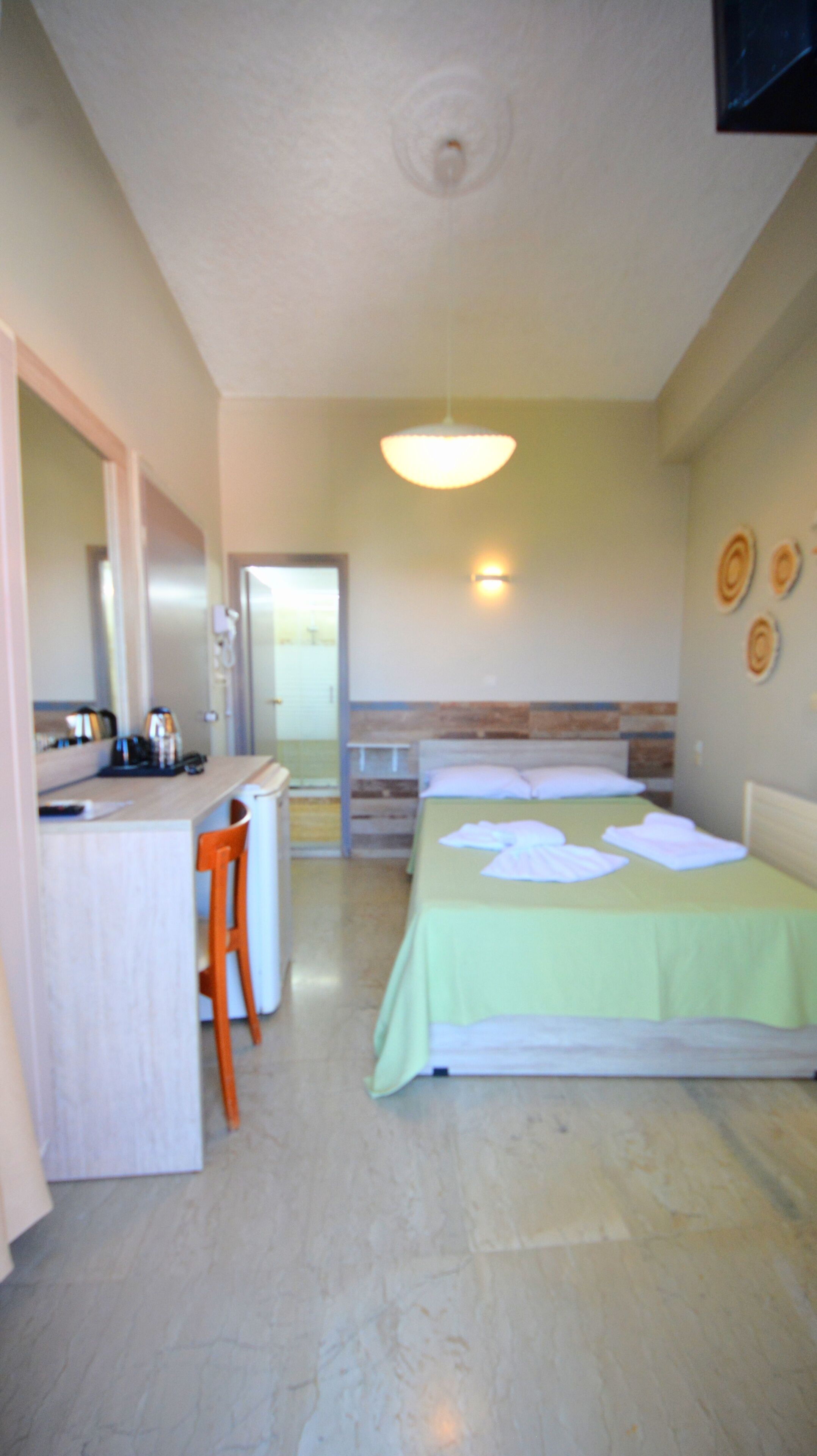Habitación de hotel con cama, escritorio y silla. Incluye refrigerador, lavamanos y espejo.
