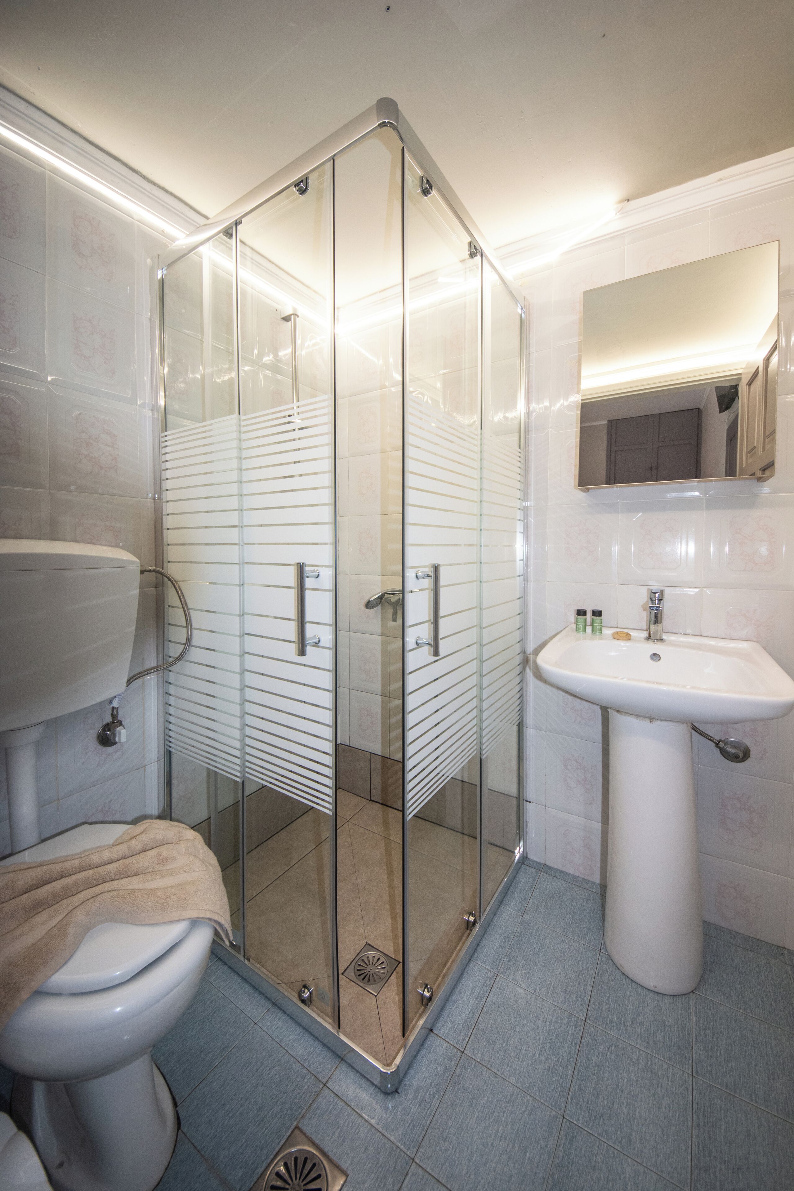 Et moderne badeværelse med en glasafskærmet brusekabine, en hvid vask og et toilet.