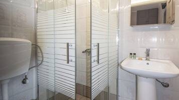 Et moderne badeværelse med en glasafskærmet brusekabine, en hvid vask og et toilet.