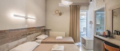 A hotel room with two beds, a small kitchenette, a mirror, and a view of the outside.