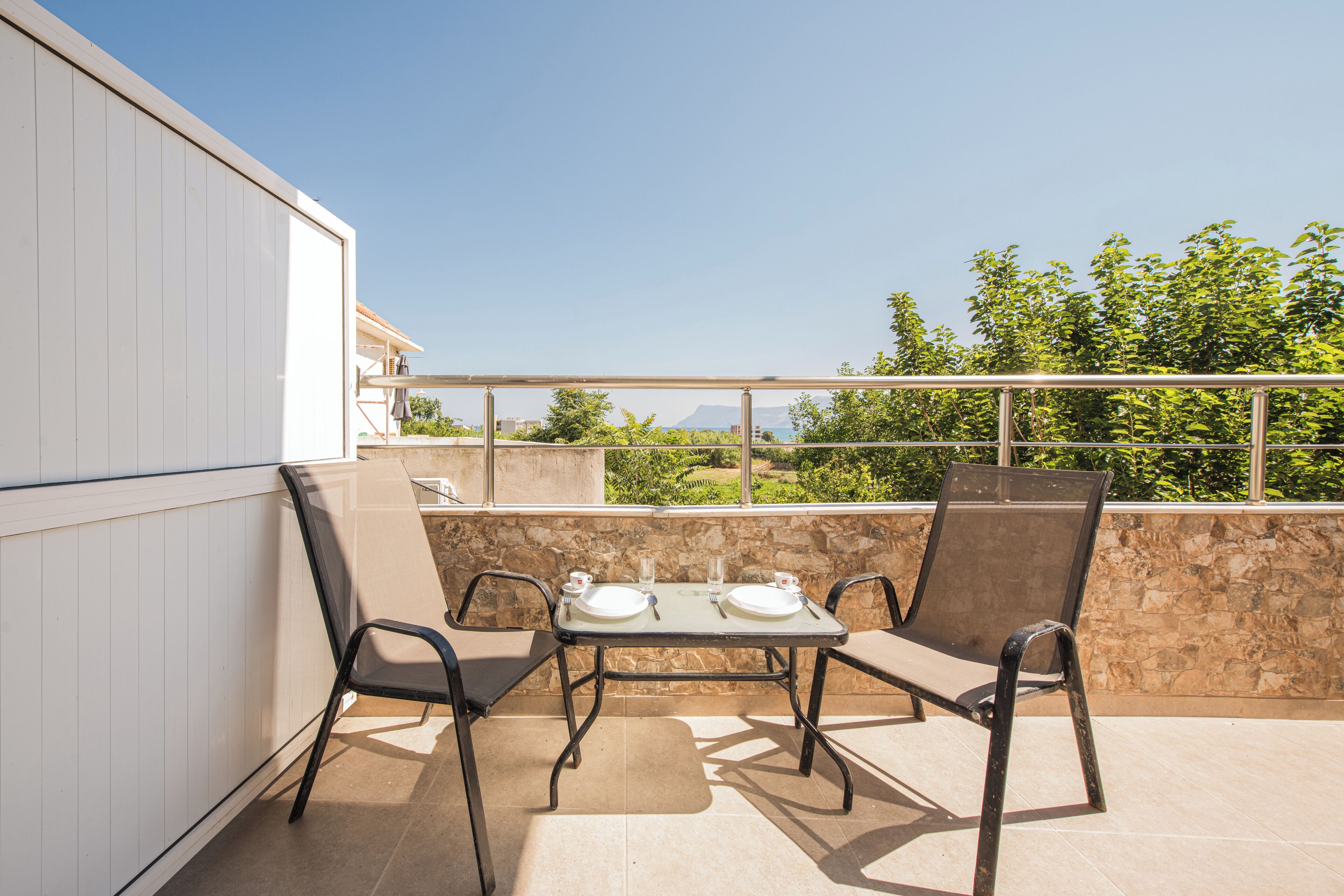 A balcony with a table set for two, chairs, and a view of the sea.
