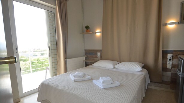 A hotel room with a large bed, a balcony, and a view of the outdoors. - Family Bikakis (Kissamos)