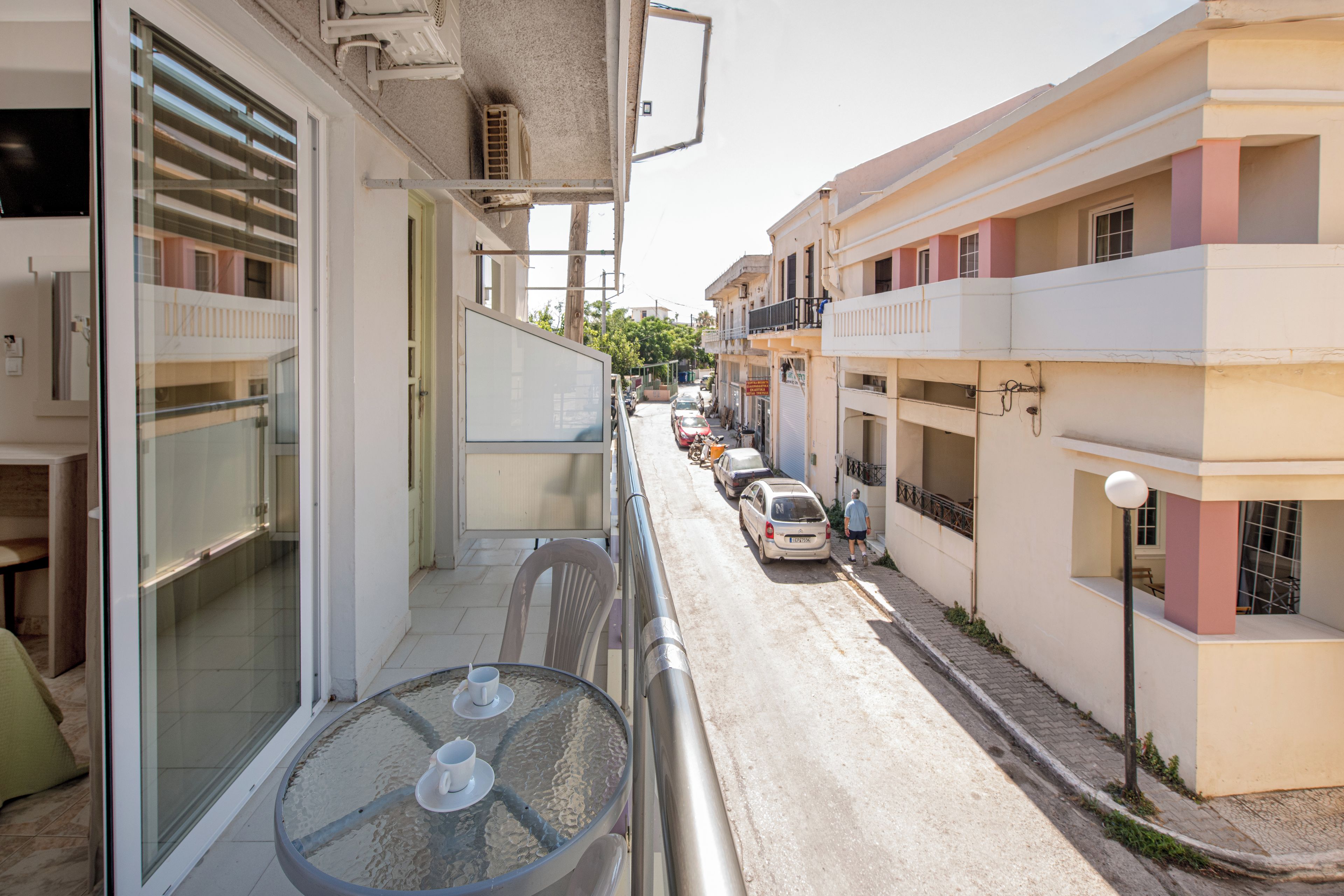 A narrow street with parked cars and buildings on either side.