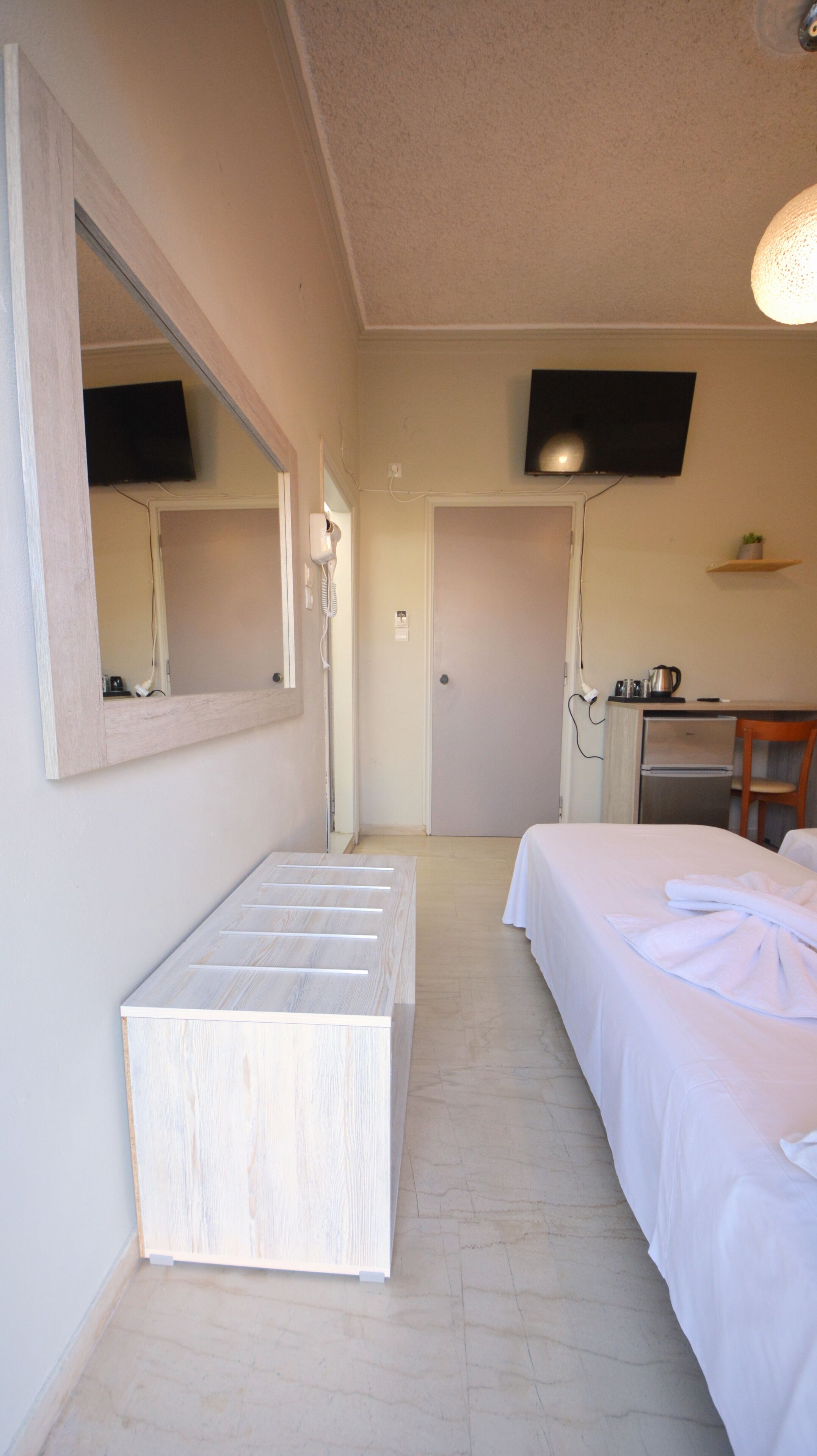 Quarto de hotel com cama, mesa de cabeceira, espelho, televisão e área de cozinha.
