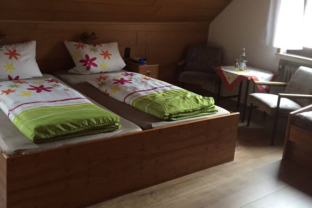 A room with two wooden beds, a small table, a chair, and a radiator.