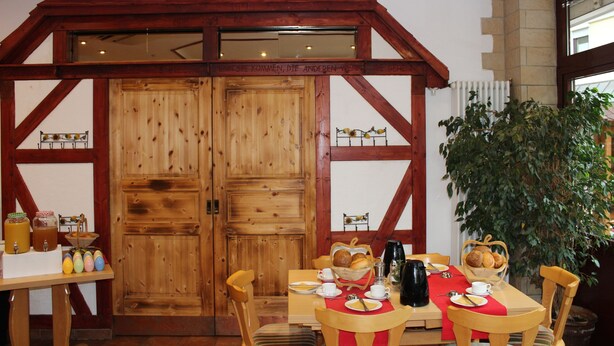 A wooden dining area with a high ceiling, wooden beams, and a large window. - Gasthof Hausmann (Schluechtern)