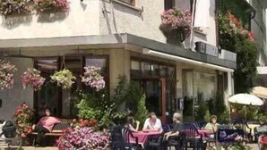 A hotel with outdoor seating, flower boxes, and a clock on the facade. - Gasthof Hausmann (Schluechtern)