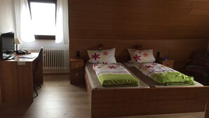 A room with two wooden beds, a desk with a computer, a chair, and a radiator. - Gasthof Hausmann (Schluechtern)