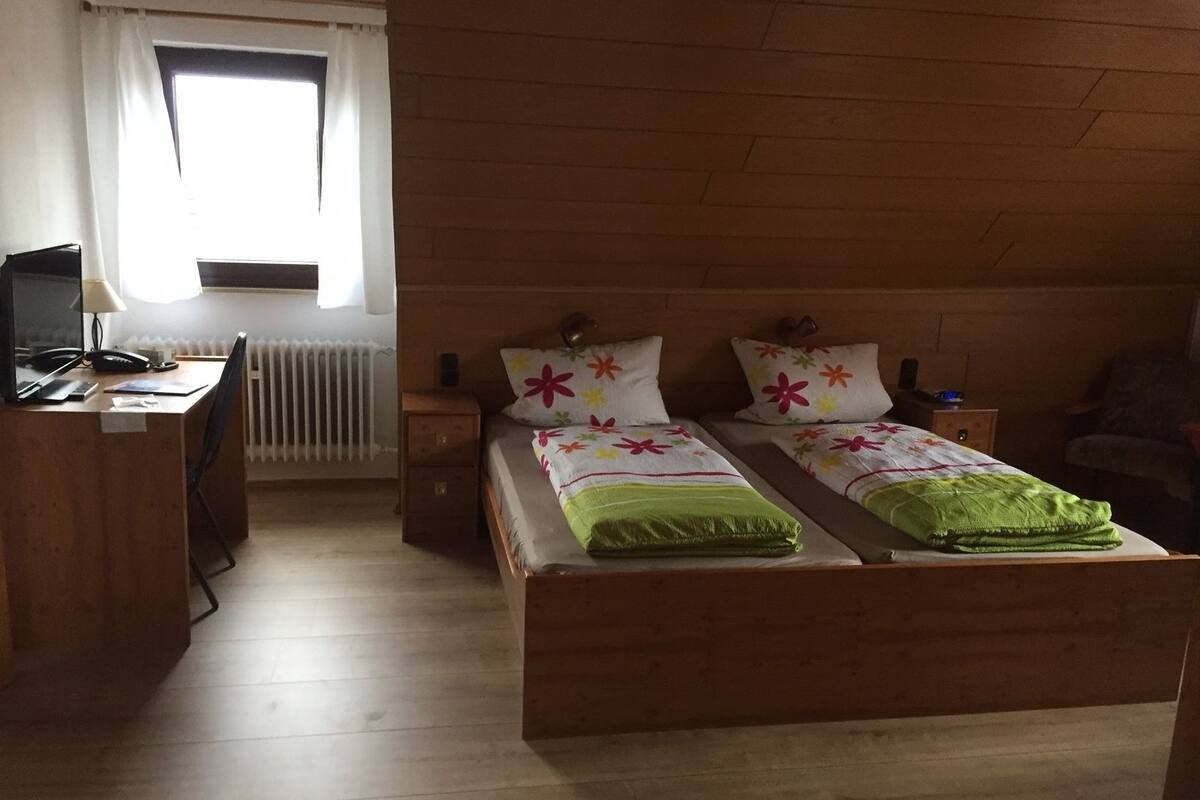 A room with two wooden beds, a desk with a computer, a chair, and a radiator.