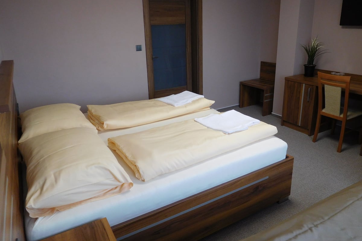 Una camera da letto con un letto in legno, due cuscini, un comodino, una sedia e un piccolo armadio.